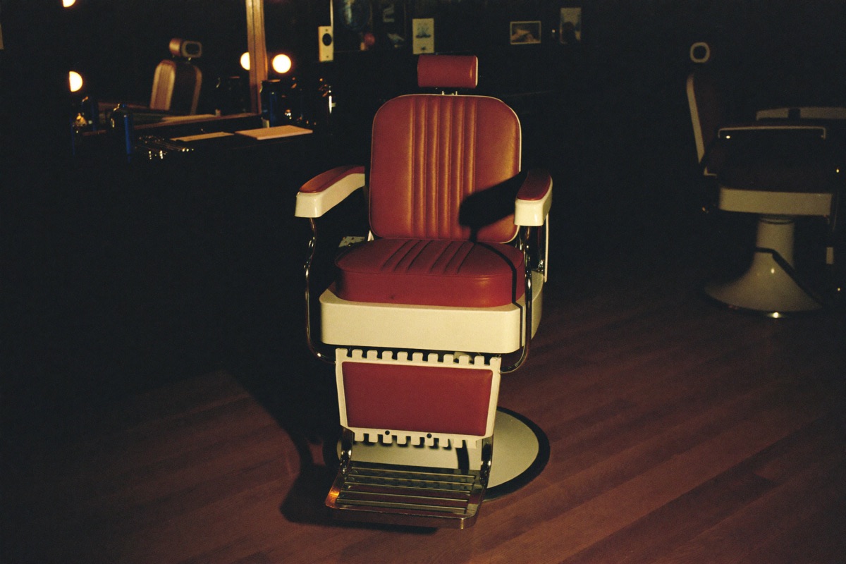 An empty red leather barber chair lit at an otherwise dark station.