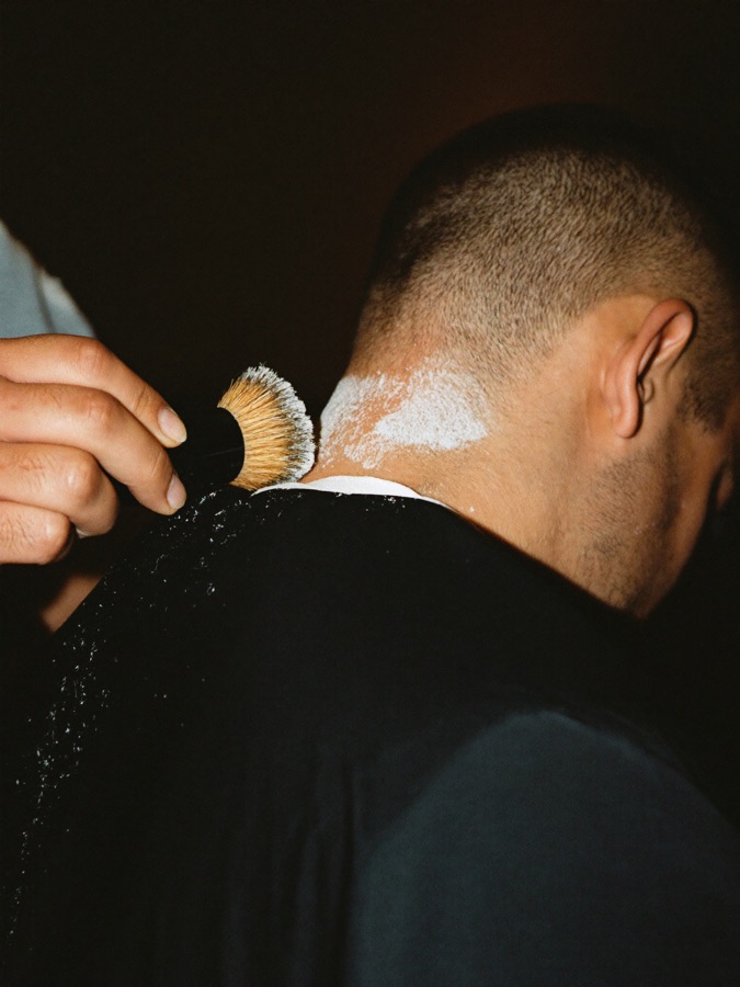 A barber dusting a freshly cut neckline with a soft horsehair brush.