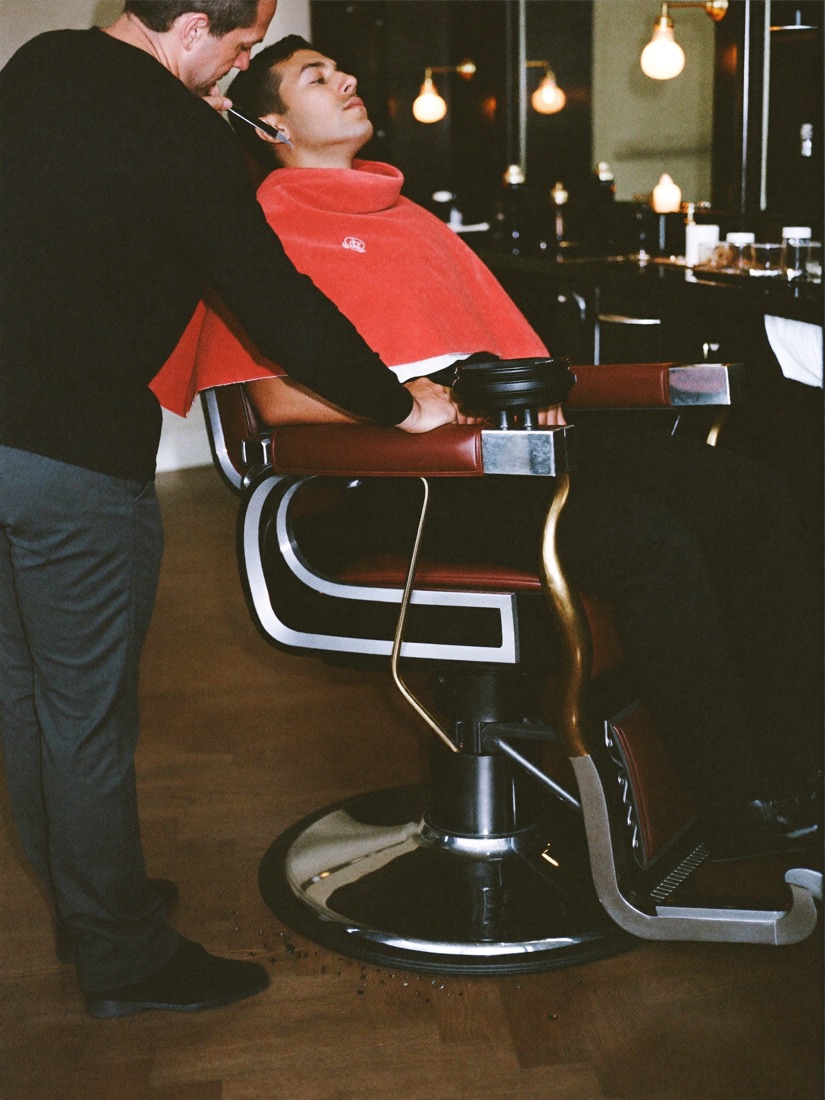 A barber holding a straight razor over a client reclined under a hot towel.